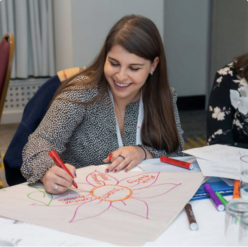 a woman smiling and writing words into a drawing of a flower